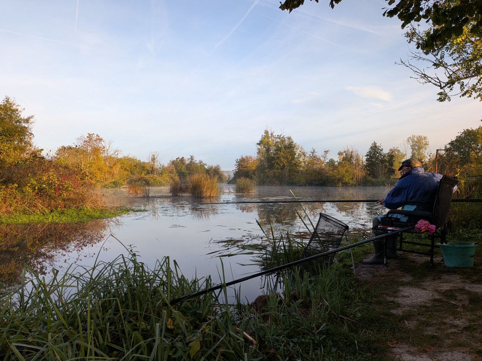 Pêcheur installé au bord de l'étang au lever du jour, en automne